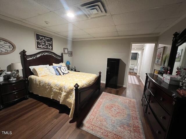 bedroom with a drop ceiling, dark wood-type flooring, and ornamental molding