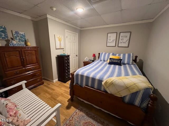 bedroom with a drop ceiling, light hardwood / wood-style floors, and ornamental molding