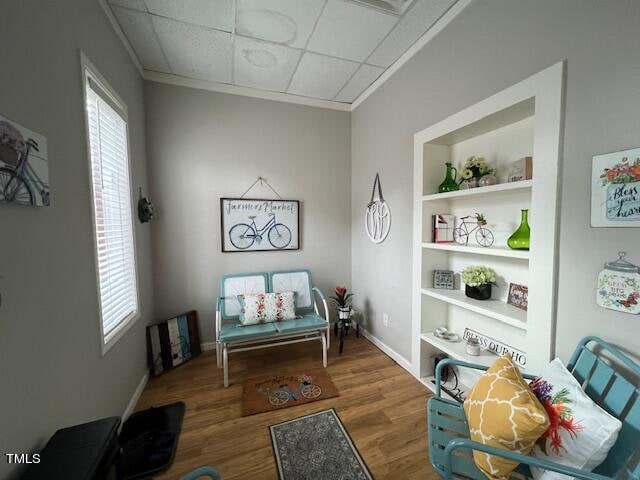 sitting room with a drop ceiling, wood-type flooring, and built in features