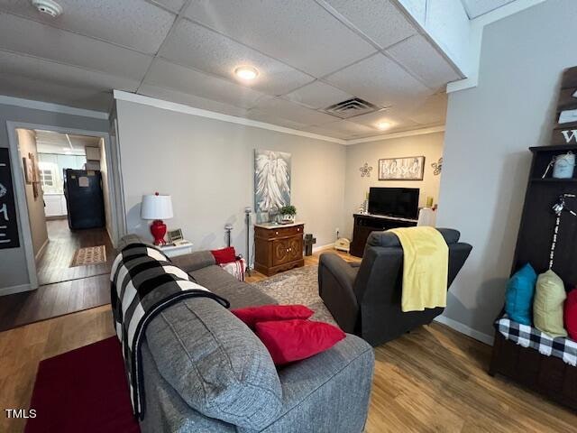 living room with a drop ceiling, wood-type flooring, and ornamental molding