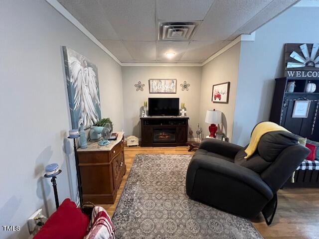 living room featuring a fireplace, crown molding, hardwood / wood-style floors, and a drop ceiling