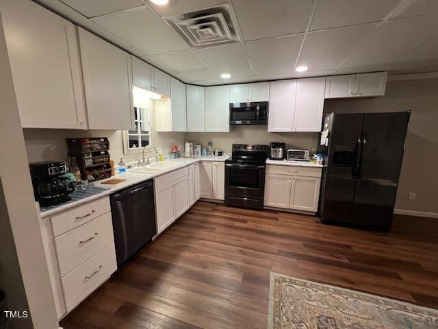 kitchen with a drop ceiling, black appliances, sink, dark hardwood / wood-style flooring, and white cabinetry