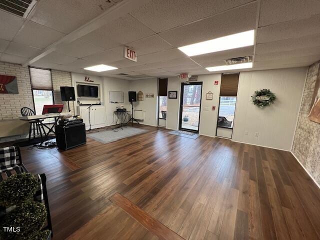 interior space with hardwood / wood-style flooring, a drop ceiling, and brick wall