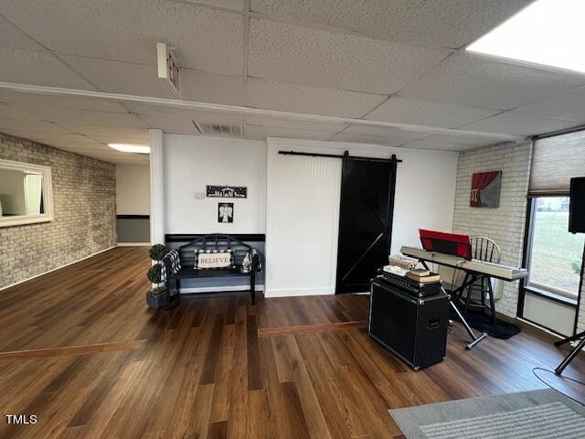 office with a drop ceiling, a barn door, dark hardwood / wood-style floors, and brick wall