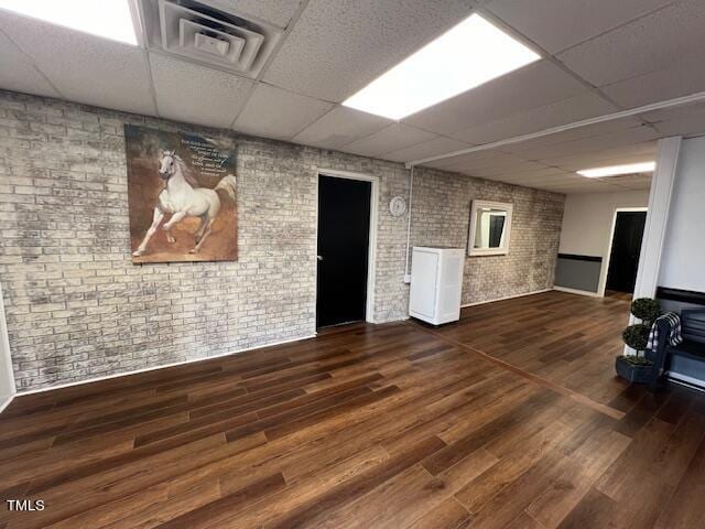 interior space featuring a paneled ceiling, dark hardwood / wood-style flooring, and brick wall