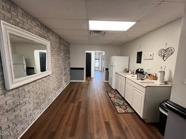 kitchen with a paneled ceiling, brick wall, white refrigerator, dark hardwood / wood-style floors, and white cabinetry