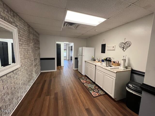 kitchen with a paneled ceiling, dark wood-type flooring, white fridge, white cabinetry, and brick wall