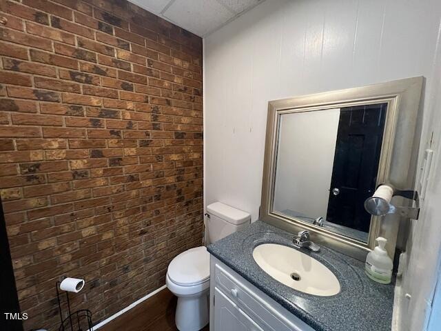 bathroom featuring hardwood / wood-style flooring, vanity, toilet, and brick wall