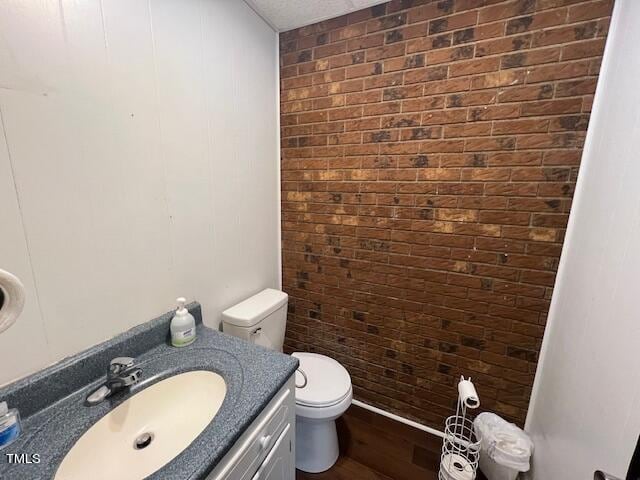 bathroom with brick wall, a textured ceiling, toilet, vanity, and hardwood / wood-style flooring