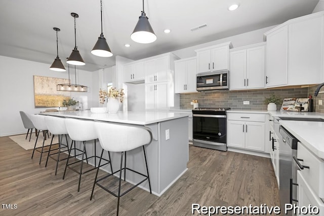 kitchen featuring hanging light fixtures, white cabinets, dark hardwood / wood-style flooring, a kitchen island, and appliances with stainless steel finishes