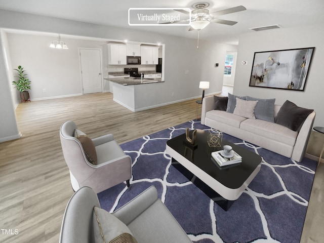 living room featuring light wood-type flooring and ceiling fan with notable chandelier