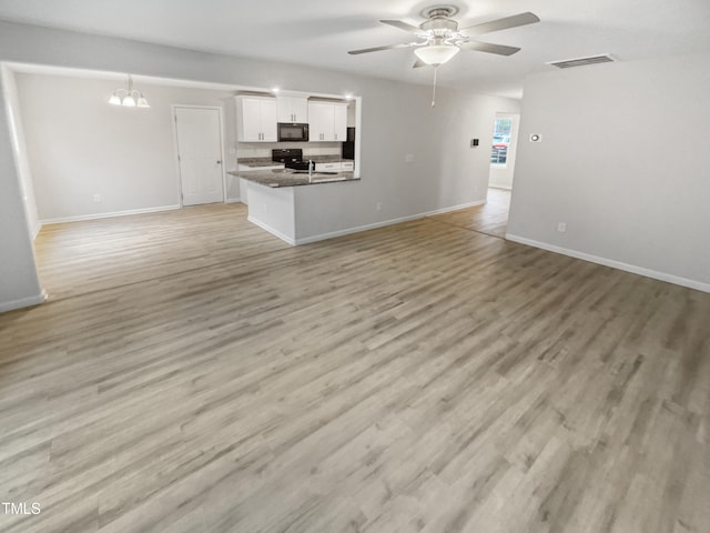 unfurnished living room featuring ceiling fan with notable chandelier and light hardwood / wood-style flooring