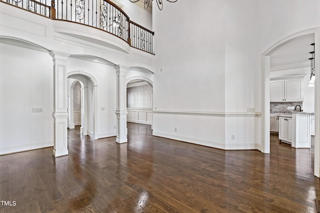 foyer entrance featuring decorative columns, dark wood-type flooring, and a towering ceiling