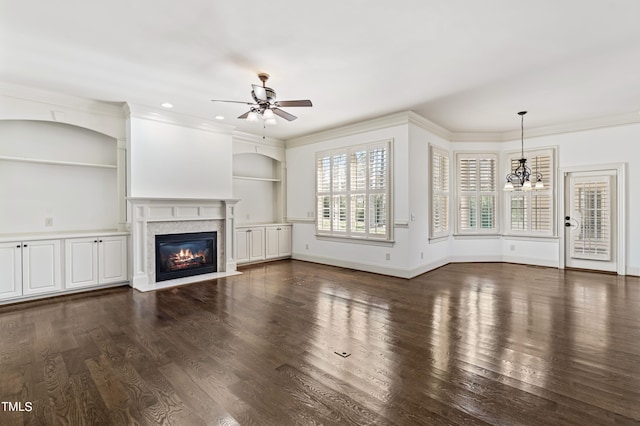 unfurnished living room featuring built in features, dark hardwood / wood-style floors, ceiling fan with notable chandelier, and a fireplace