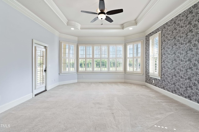 carpeted spare room featuring a tray ceiling, ornamental molding, ceiling fan, and a wealth of natural light