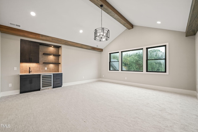 unfurnished living room featuring vaulted ceiling with beams, wine cooler, indoor wet bar, light colored carpet, and a notable chandelier