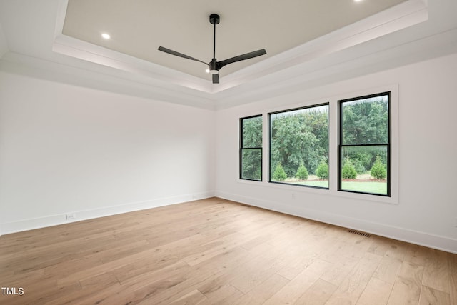 empty room with a tray ceiling, light hardwood / wood-style floors, and ceiling fan