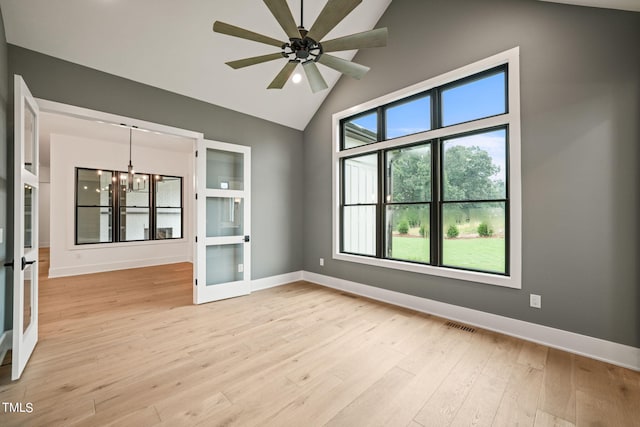 spare room with french doors, ceiling fan with notable chandelier, lofted ceiling, and light wood-type flooring