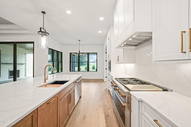 kitchen with light stone counters, white cabinets, sink, appliances with stainless steel finishes, and light wood-type flooring