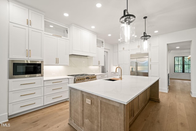 kitchen with light stone counters, built in appliances, white cabinets, hanging light fixtures, and a center island with sink