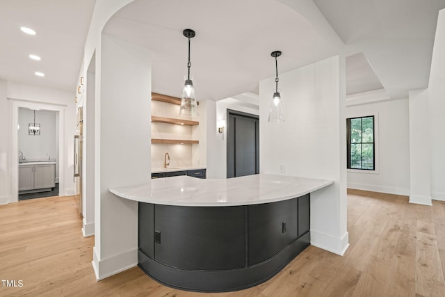 kitchen featuring light hardwood / wood-style flooring, kitchen peninsula, decorative light fixtures, and sink