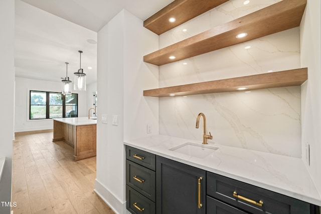 bar featuring pendant lighting, sink, light hardwood / wood-style flooring, backsplash, and light stone countertops