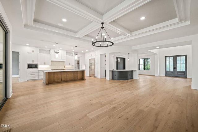 unfurnished living room featuring light wood-type flooring, beam ceiling, coffered ceiling, and french doors