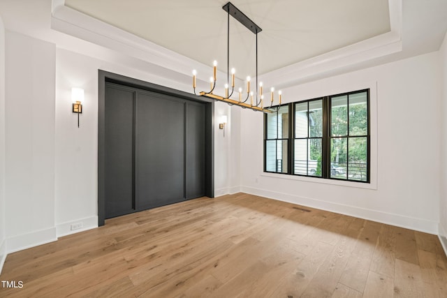 unfurnished room with an inviting chandelier, a tray ceiling, and light hardwood / wood-style floors