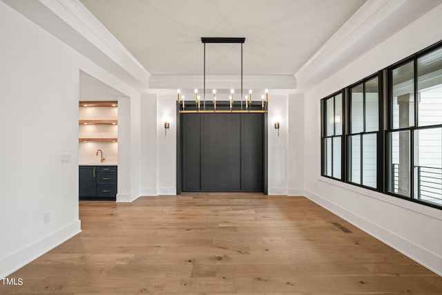 unfurnished dining area featuring an inviting chandelier, light hardwood / wood-style floors, ornamental molding, and sink