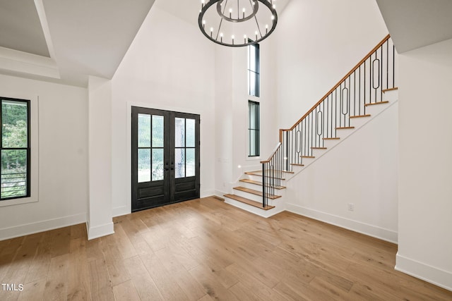 foyer entrance featuring french doors, an inviting chandelier, light wood-type flooring, and a high ceiling