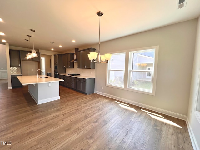 kitchen with sink, wall chimney range hood, tasteful backsplash, pendant lighting, and a kitchen island with sink