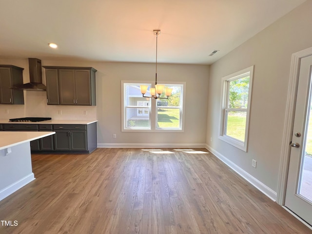 kitchen featuring wall chimney range hood, hanging light fixtures, a chandelier, light hardwood / wood-style floors, and gas cooktop