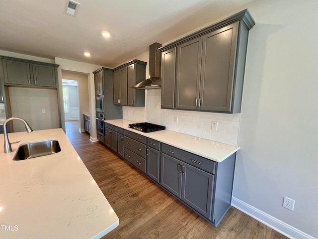 kitchen featuring sink, dark wood-type flooring, wall chimney range hood, tasteful backsplash, and appliances with stainless steel finishes