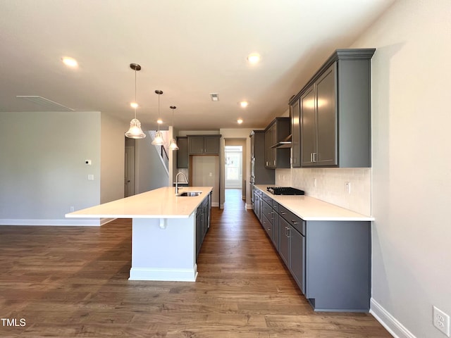 kitchen featuring sink, dark hardwood / wood-style floors, backsplash, pendant lighting, and a center island with sink