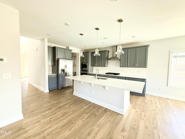 kitchen with pendant lighting, sink, stainless steel refrigerator with ice dispenser, wall chimney exhaust hood, and light hardwood / wood-style floors