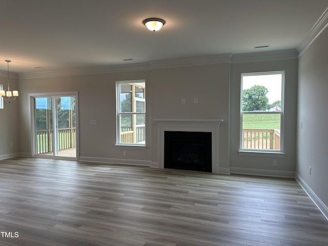 unfurnished living room featuring hardwood / wood-style floors, ornamental molding, plenty of natural light, and a notable chandelier