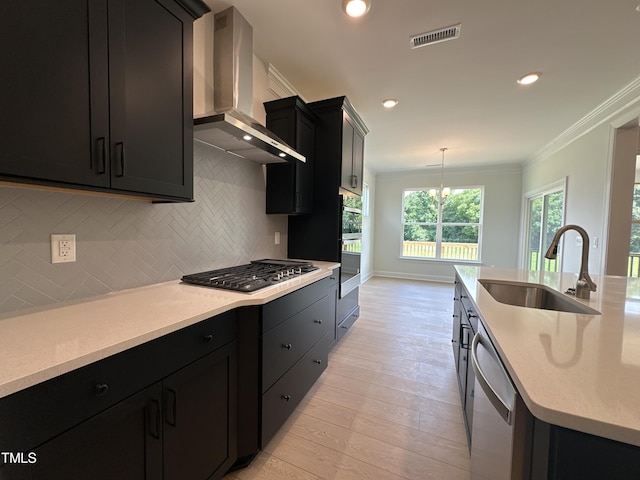 kitchen featuring pendant lighting, appliances with stainless steel finishes, wall chimney range hood, sink, and crown molding