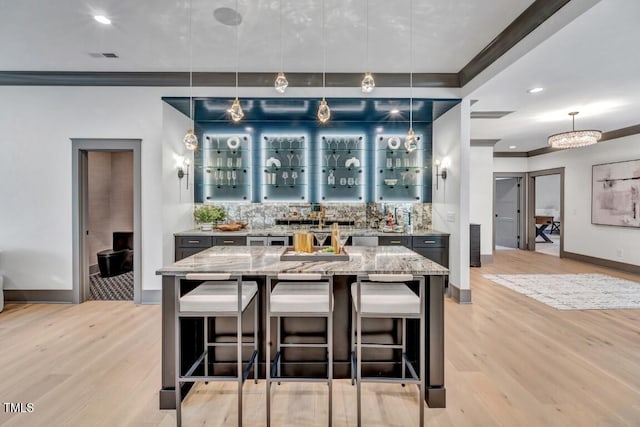 1312 Hunting Ridge Rd, Raleigh, NC 27615 - kitchen featuring light wood-style flooring, light stone counters, decorative backsplash, ornamental molding, and a kitchen bar