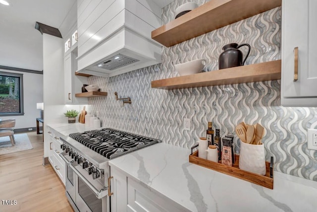 kitchen with white cabinetry, light stone countertops, light hardwood / wood-style floors, range with two ovens, and custom exhaust hood