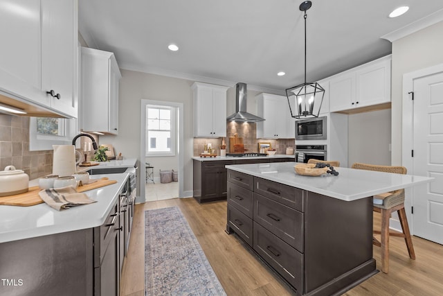 kitchen featuring a kitchen island, pendant lighting, white cabinets, stainless steel appliances, and wall chimney exhaust hood