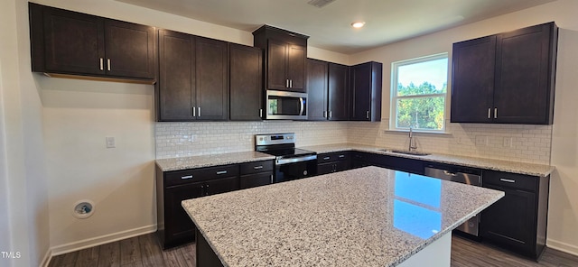 kitchen with a kitchen island, dark hardwood / wood-style floors, sink, appliances with stainless steel finishes, and light stone counters