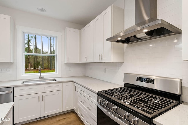 kitchen featuring appliances with stainless steel finishes, white cabinets, light hardwood / wood-style flooring, wall chimney exhaust hood, and backsplash