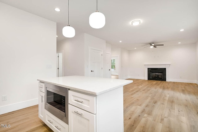 kitchen with decorative light fixtures, white cabinetry, stainless steel microwave, ceiling fan, and light wood-type flooring