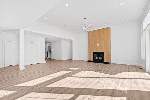 unfurnished living room with crown molding, a large fireplace, an inviting chandelier, and light hardwood / wood-style flooring