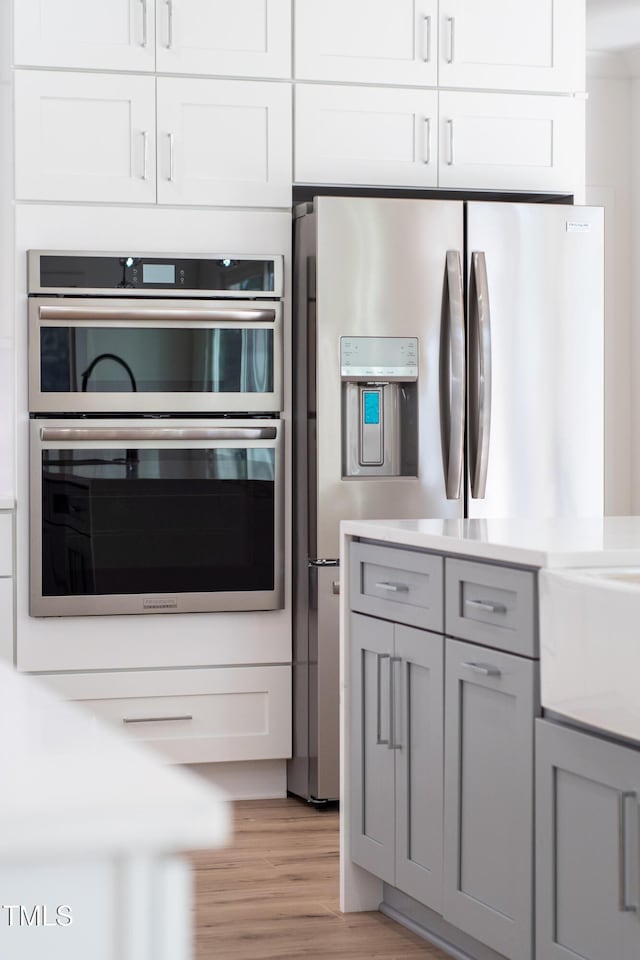 kitchen featuring white cabinets, appliances with stainless steel finishes, light hardwood / wood-style flooring, and gray cabinetry