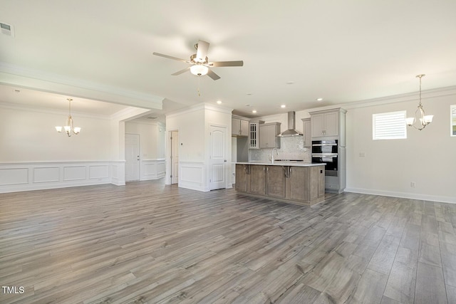 kitchen with a kitchen island, light wood-type flooring, wall chimney range hood, and hanging light fixtures