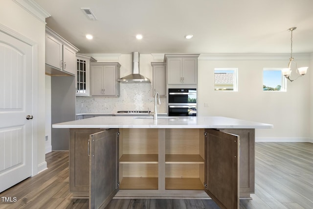 kitchen featuring hardwood / wood-style floors, wall chimney exhaust hood, sink, and an island with sink