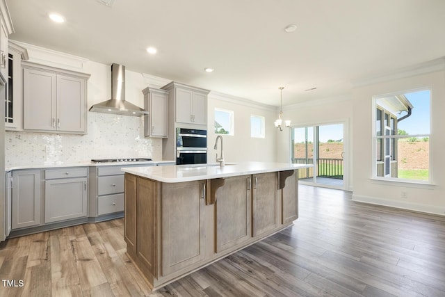 kitchen featuring gas cooktop, a kitchen breakfast bar, wall chimney exhaust hood, light hardwood / wood-style flooring, and an island with sink