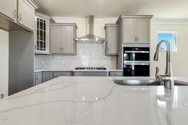 kitchen with gray cabinets, light stone counters, wall chimney range hood, and appliances with stainless steel finishes