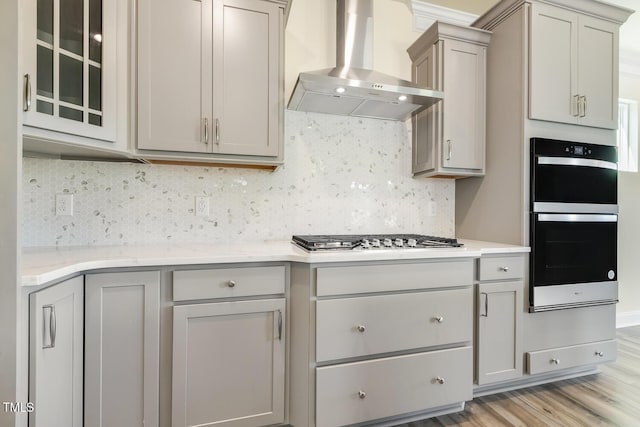 kitchen featuring stainless steel appliances, gray cabinets, wall chimney exhaust hood, and light hardwood / wood-style floors